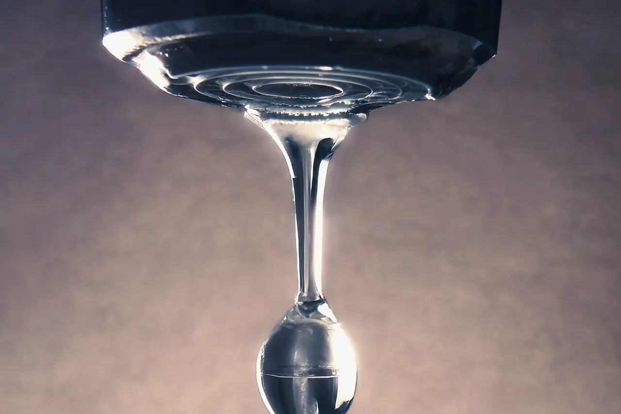 A single drop of water forming at the tip of a faucet.
