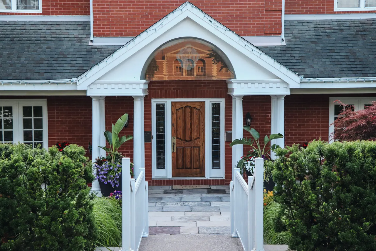 The front entry of a red-brick house, with a white portico and a wooden door.