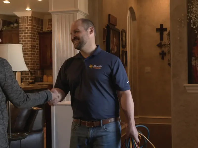 A technician in a navy company polo shakes hands with a homeowner inside the front door of a house.