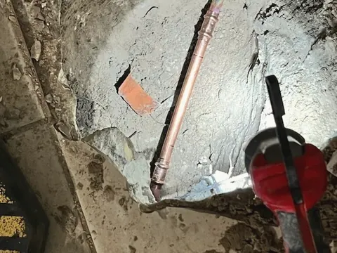 A hole cut through a concrete slab exposes a copper water line during a leak repair.