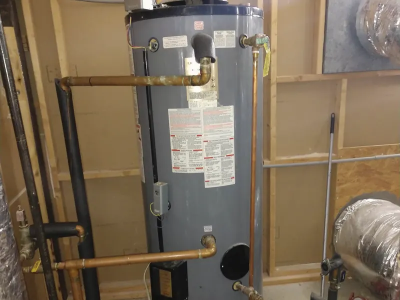 A newly installed tall gas water heater with copper piping in a utility room.