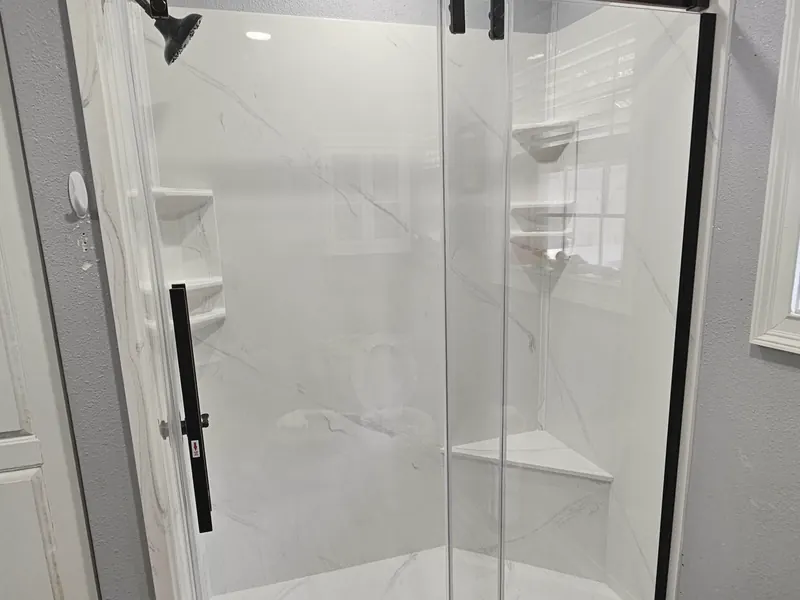 A finished walk-in shower with a sliding glass door and white marble-look walls.