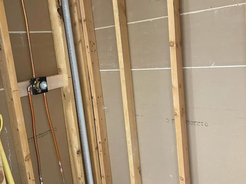 Copper supply lines and a shower valve roughed in on a framed wall before drywall.