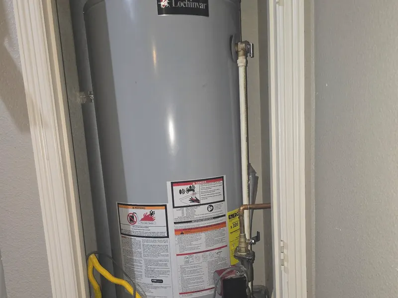 A gas water heater installed in a closet, with a yellow gas line and an expansion tank above.