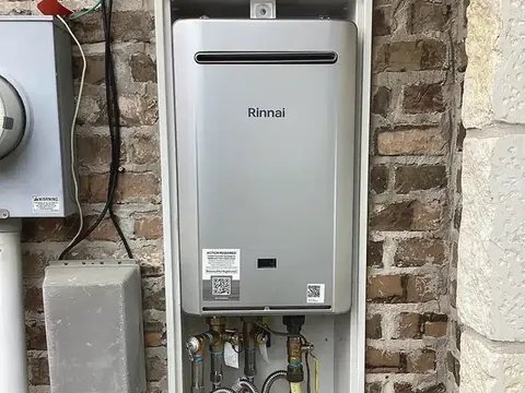 A tankless water heater installed in a recessed box on a brick outside wall.