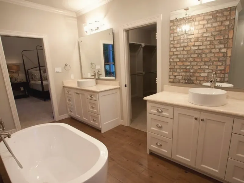 A finished main bathroom with a freestanding tub, two vessel-sink vanities and a brick accent wall.