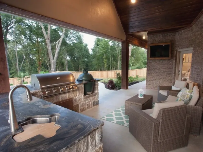 A covered patio with an outdoor kitchen sink set in a stone counter beside a grill.